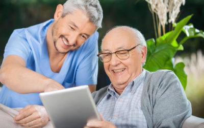 Happy male nurse and senior man enjoying while using tablet computer in nursing home porch